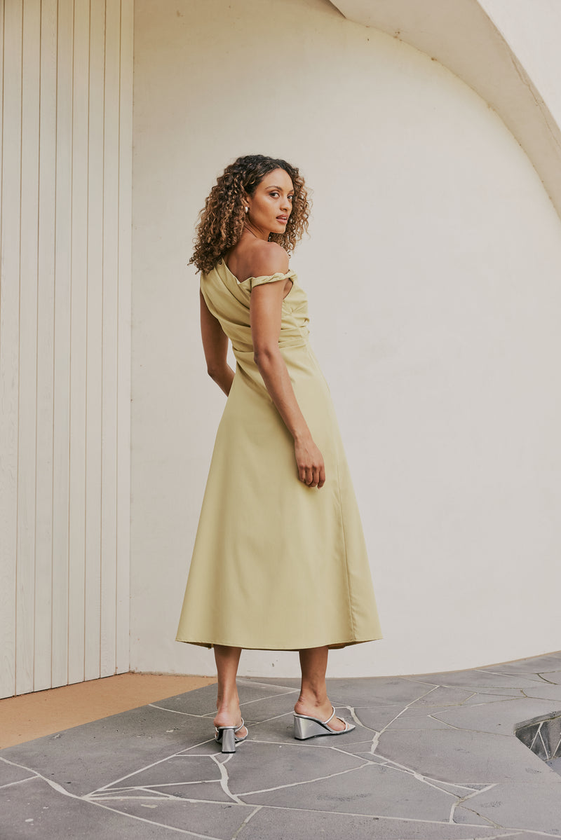 Brunette Model wears CURAAE Elenor Asymmetrical Summer Midi Dress In Olive back shot 