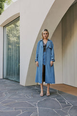 blonde model wears CURAAE Aurora Long Denim Textured Tie Trench In Mid Blue front shot