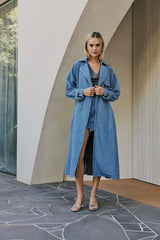 blonde model wears CURAAE Aurora Long Denim Textured Tie Trench In Mid Blue front shot