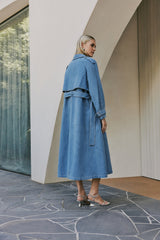 blonde model wears CURAAE Aurora Long Denim Textured Tie Trench In Mid Blue back shot