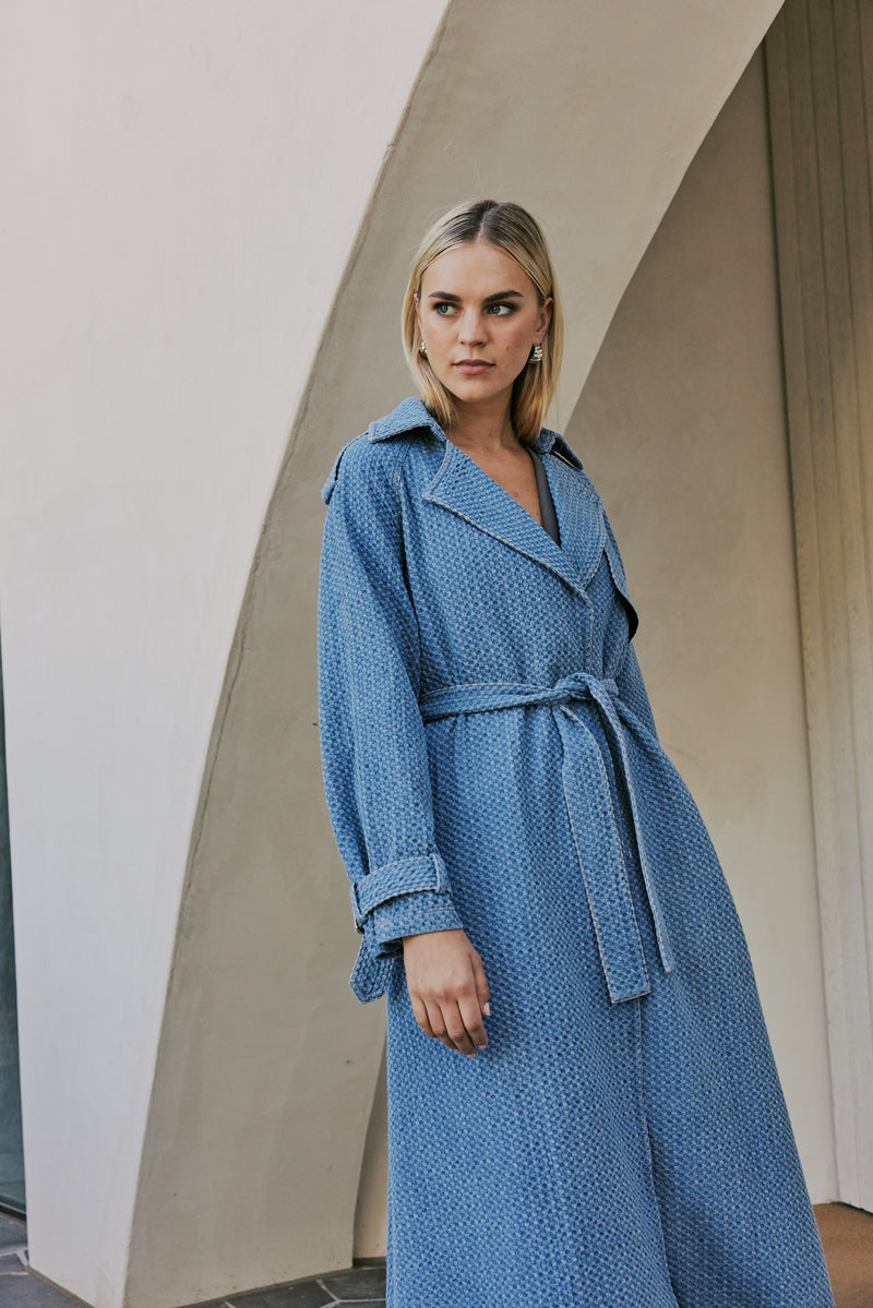 blonde model wears CURAAE Aurora Long Denim Textured Tie Trench In Mid Blue close up shot