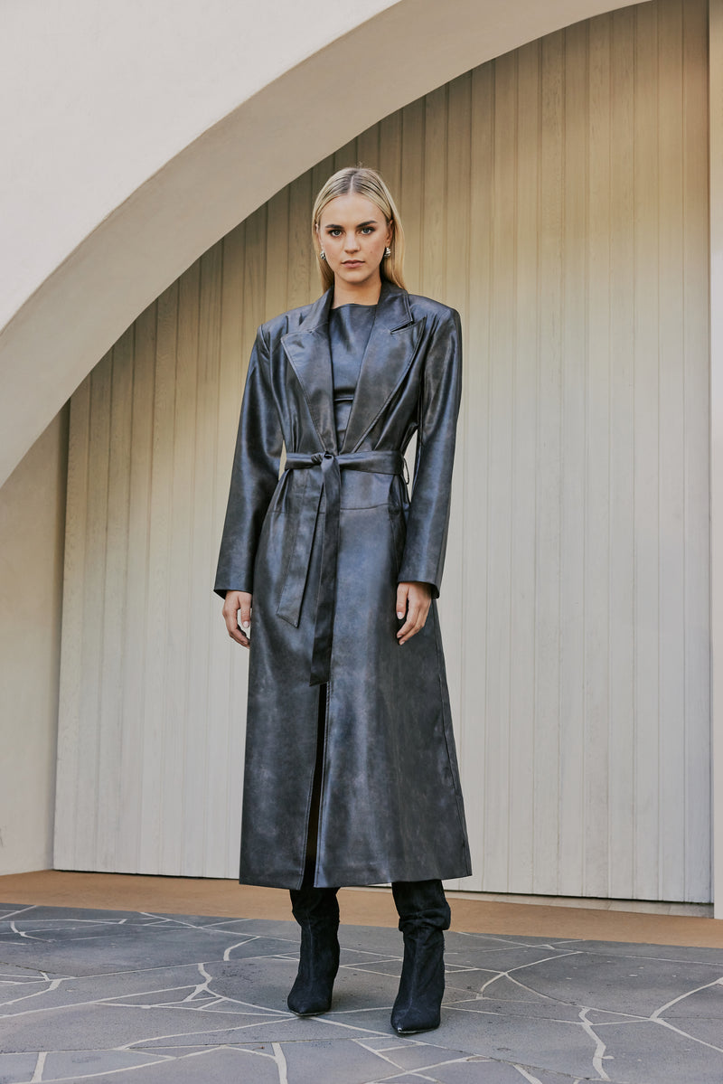 blonde model wears boots and leather mini dress and CURAAE Cameron Vegan Leather Fabric Tie Trench Coat In Chestnut front shot 