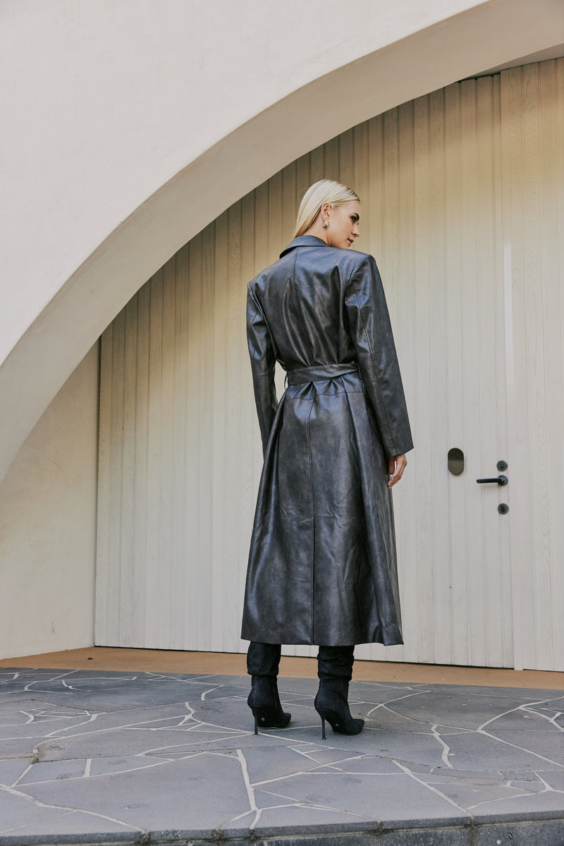 blonde model wears boots and leather mini dress and CURAAE Cameron Vegan Leather Fabric Tie Trench Coat In Chestnut  back shot