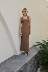 blonde model wears with gold earrings and strappy heals on cream wall CURAAE Quinn Textured Mermaid Flared Tank Maxi Dress In Coco front shot